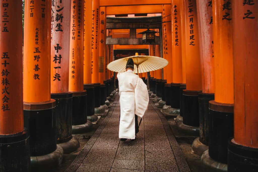 A person in traditional attire walks through the iconic torii gates at Fushimi Inari Shrine, Kyoto.